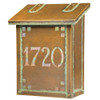 A vertical brass mailbox with an aged patina finish, glass corner accents and address numbers on the front backed by glass. 