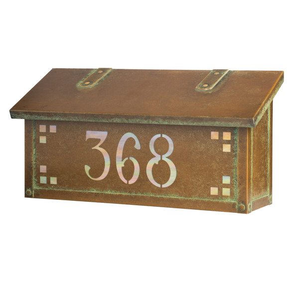 A horizontal brass mailbox with an aged patina finish, glass corner accents and address numbers on the front backed by glass. 