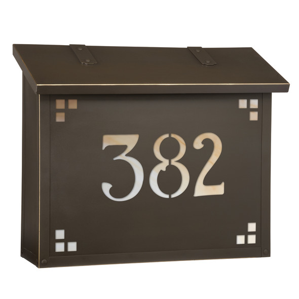 A large brass mailbox with a bronze finish, glass corner accents and address numbers on the front backed by glass. 