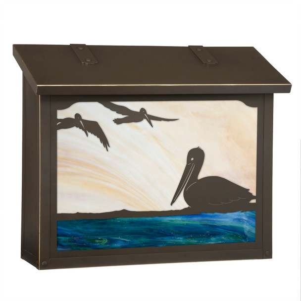 A large brass mailbox with a bronze finish, warm toned glass and artwork featuring a trio of pelicans on the ocean. 