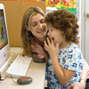 A child and teacher sitting in front of a computer with a Jelly Beamer Transmitter on the table