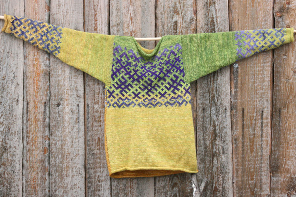 Chartreuse Green Latvian symbols reversible unisex sweater knit by Wrapture by Inese and hung flat on side of woodshed size M