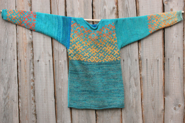 Turquoise blue Latvian symbols reversible sweater flat on side of woodshed size L
