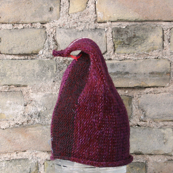 Latvia S/M pixie gnome hat knit by Wrapture by Inese in front of brick wall