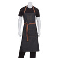 Dark indigo denim bib apron with tan leather straps, chest pocket, and twin waist pockets, worn by male model