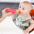 Baby in high chair being fed with a coral pink silicone food dispensing spoon