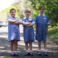 Three children wearing royal blue gingham check school dresses with white Peter Pan collars and chest pockets