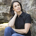 Woman seated outdoors wearing a black short-sleeve polo shirt with button placket and classic collar