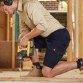 Man kneeling on timber frame using drill, wearing navy cotton canvas cargo shorts with side pockets on worksite