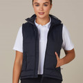 Woman wearing navy padded vest with high collar, front zip, and side pockets over white polo