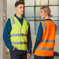 Front and back view of hi-vis safety vests with reflective tape in fluorescent yellow and orange worn over teal long sleeve shirts