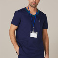 Man wearing navy short-sleeve scrub top with teal contrast V-neck trim, chest pen pocket and lanyard