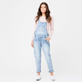 Model wearing pale blue washed denim maternity overalls with adjustable straps, chest bib pocket and rolled cuffs