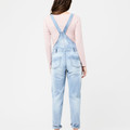 Back view of pale blue denim overalls with crossover straps and twin back pockets, worn by a model
