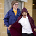 Two kids wearing navy and maroon all-weather jackets with hoods, styled over school uniforms outdoors