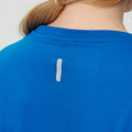 Close-up back view of cobalt blue textured performance tee on female model, showing reflective tab detail at upper back