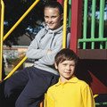 Child wearing navy track pants with reinforced knee panels and grey hoodie, beside child in golden yellow polo shirt