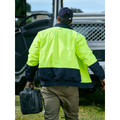 Man wearing hi vis yellow and navy two-tone waterproof bomber jacket, rear view, worksite setting