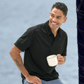 Man wearing black jacquard knit polo with three-button placket, holding a ceramic mug in casual setting