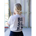 Woman wearing light grey marle cotton tee with large navy vertical logo print across the back, worksite setting