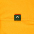 Close-up of amber cotton polo dress showing bottle green placket patch with metal button detail