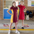 Two girls in school setting wearing polo dresses — maroon with gold panels and red with black side panels, polo collar