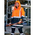 Woman on construction site wearing orange and navy hi vis rain jacket with hood up and reflective tape in rain