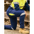 Woman kneeling on worksite in navy ripstop cargo pants with yellow hi-vis panels and reflective tape at knee