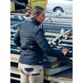 Woman in navy quilted puffer jacket with stand collar working outdoors at a metal rack