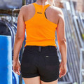 Woman wearing bright orange racerback singlet and black mid-rise stretch shorts, rear view, outdoor worksite setting