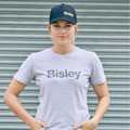 Woman wearing navy five-panel baseball cap with gold embroidered logo, paired with grey marle tee