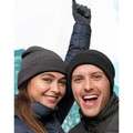 Two models outdoors wearing charcoal and black ribbed knit roll-up beanies with winter jackets