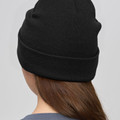Black ribbed knit beanie with fold-up cuff worn by model, rear view showing clean crown panel
