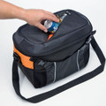 Hand placing can into open black and orange 20L cooler bag with shoulder strap, mesh side pocket and silver piping