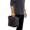 Black insulated cooler bag with top handle and structured rectangular shape held by person in grey shirt