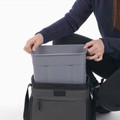Person lifting grey insulated container from Charcoal 16-can cooler bag with zip front pocket and shoulder strap