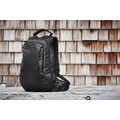 Black waterproof commuter backpack with structured panels and top carry handle against rustic timber wall