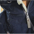 Close-up of navy softshell jacket with water droplets on surface, branded metal zip pull and contrast cream lining at collar