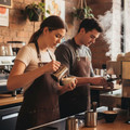 Canvas apron in brown with brass eyelets and tan adjustable straps worn by baristas in café setting