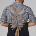 Tan cross-back apron straps with tie closure over navy and white gingham checked shirt