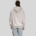 Back view of model wearing an oversized sand pullover hoodie with ribbed hem and dropped shoulders