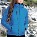 Woman wearing cobalt blue lightweight puffer jacket with hood, contrast zip details and quilted panels, rocky coastal backdrop