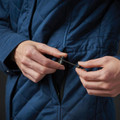 Close-up of hands zipping a navy blue quilted insulated jacket pocket with black zip pull