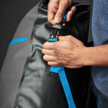 Hands fastening black buckle on charcoal waterproof roll-top backpack with electric blue webbing strap