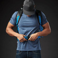 Model wearing Stormtech 40L waterproof roll-top backpack in cyan and black with chest strap fastened