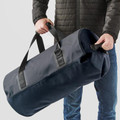 Model holding large navy blue waterproof duffel bag with welded seams and black carry handles