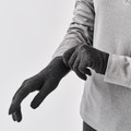 Model pulling on charcoal grey knit gloves with full finger coverage over a light grey long-sleeve top