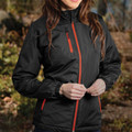 Woman wearing black insulated jacket with red contrast zip trim, zippered chest pocket, elasticated cuffs, outdoor setting