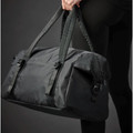 Charcoal grey 32L nylon duffle bag with buckle straps and zip pocket held by model in black