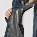 Close-up of slate blue technical shell jacket interior showing taped seams, perforated grey lining, and waterproof membrane construction